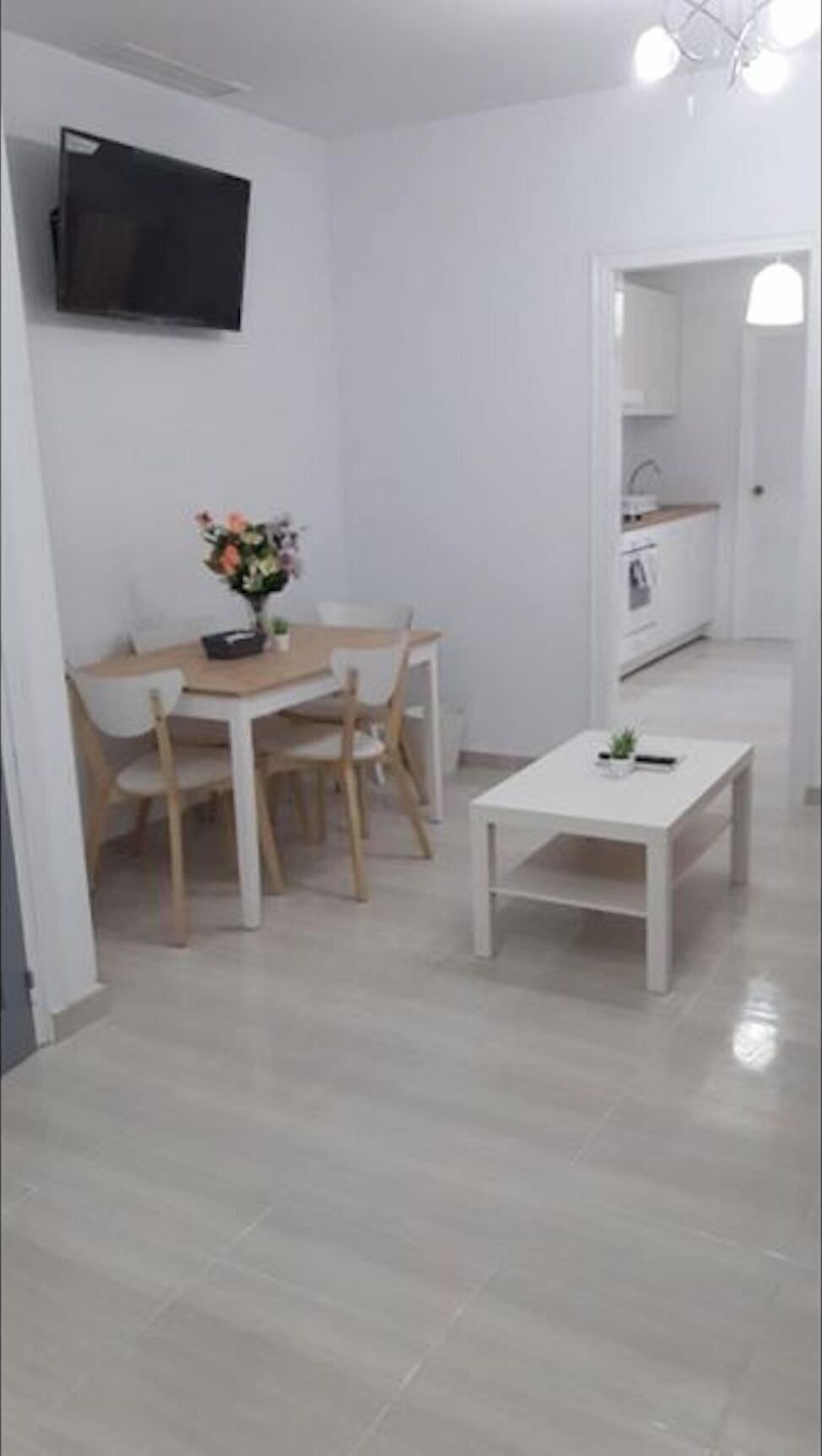 Un petit espace de vie moderne comprenant un coin repas, une cuisine et un téléviseur fixé au mur.