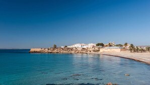 Une ville côtière avec des bâtiments qui bordent le rivage, une eau d’un bleu limpide et une plage rocheuse.