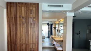Un couloir d’hôtel avec une cloison en bois, une salle de bain avec deux lavabos et des miroirs, et un téléphone fixé au mur.