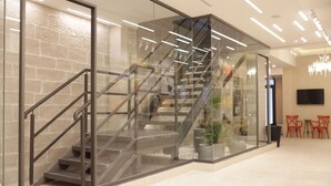 Un intérieur moderne avec un escalier à parois de verre, un lustre et des chaises rouges.