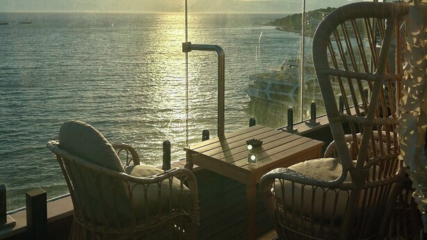 Une terrasse avec des chaises et une table en osier, donnant sur une étendue d’eau au coucher du soleil.