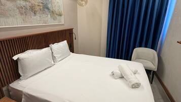 Una habitación de hotel con una cama, una silla, una obra de arte en la pared y un ventanal con cortinas.