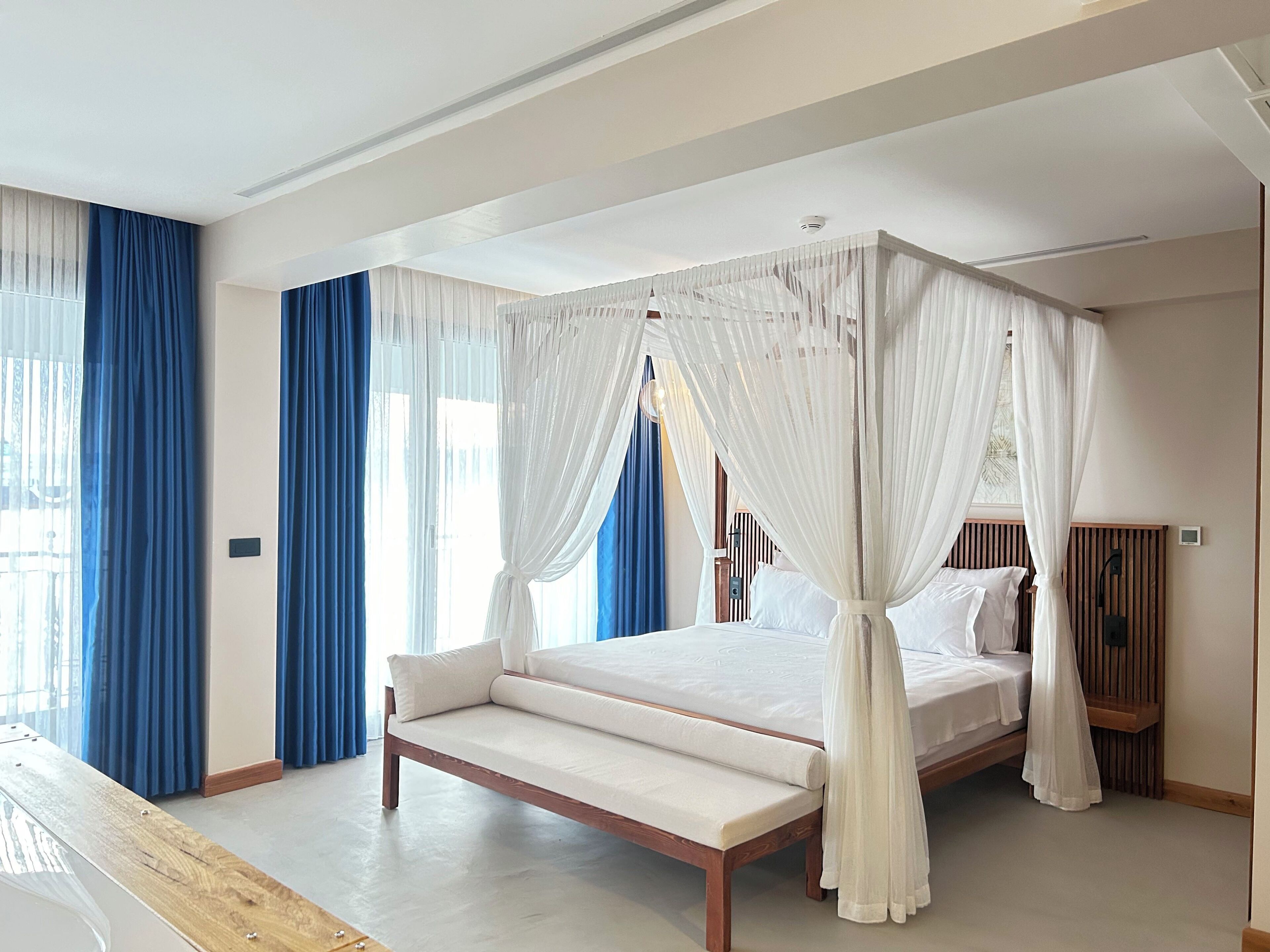 A bedroom with a four-poster canopy bed, a wooden bench, and a nightstand with a lamp.