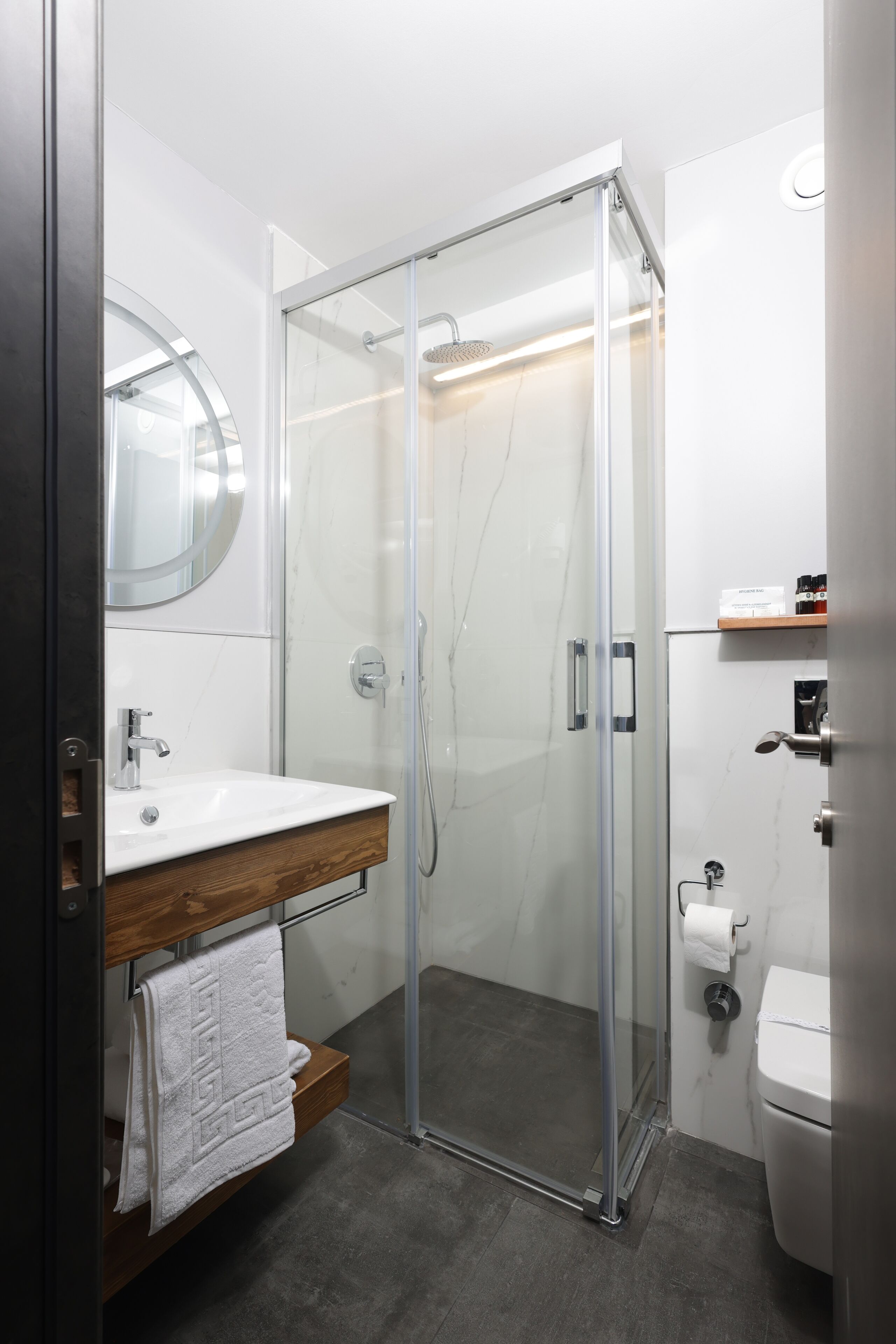 A modern bathroom with a glass-enclosed shower, a wooden vanity, a white sink, and a toilet.