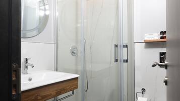 A modern bathroom with a glass-enclosed shower, a wooden vanity, a white sink, and a toilet.