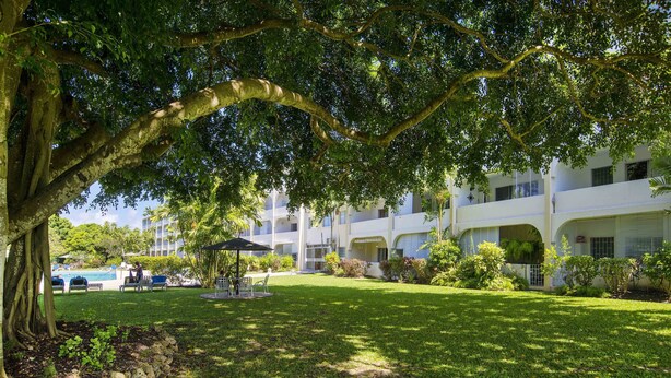 En frodig have med en pavillon, en swimmingpool og en bygning med flere balkoner.