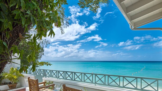 A wooden deck with a table and chairs, overlooking a turquoise sea with a clear sky. - Southwinds - by ZenBreak (Mullins)