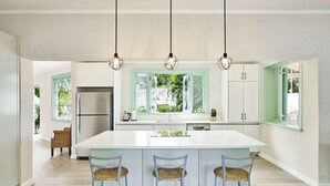 A modern kitchen with a large island, three bar stools, and pendant lighting. - Southwinds - by ZenBreak (Mullins)