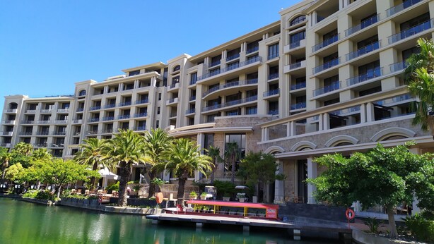 Un hôtel à plusieurs étages, doté de balcons, avec un plan d’eau devant et un petit quai pour bateaux.
