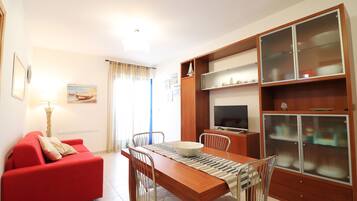 A compact living space with a dining area, a red sofa, a TV, and a cabinet with glass doors.