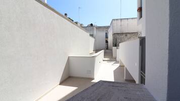 Uma passagem estreita e ensolarada entre edifícios, com uma rampa de concreto que dá acesso a uma escadaria.