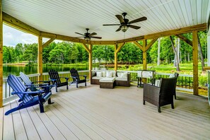 Une terrasse extérieure couverte, dotée de chaises Adirondack et de meubles en osier, avec vue sur un lac.