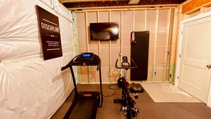 Une salle de sport à domicile équipée d’un tapis de course, d’un vélo d’appartement et d’un téléviseur fixé au mur.