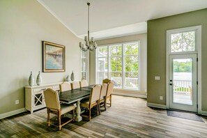 A dining room with a large table and chairs, a chandelier, a painting, and a view through large windows. - 250’ of Lakefront with Boat House & Private Beach (Mineral)