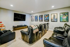 A home theater room with a flat-screen TV, reclining chairs, a popcorn machine, and movie posters on the wall.