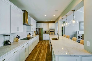 Una cocina moderna con armarios blancos, una isla grande, electrodomésticos de acero inoxidable e iluminación colgante.