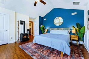 A bedroom with a bed, a fireplace, a blue accent wall, a round mirror, and a nightstand with a lamp. - Huge 8BR Lakefront Lake Anna, Beach, Dock, Hot Tub (Bumpass)