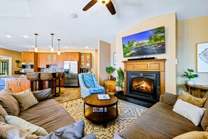 Una sala de estar moderna con chimenea, un televisor montado en la pared y una cocina al fondo.