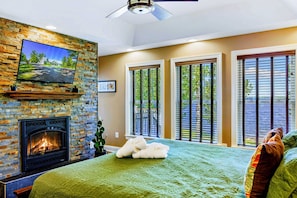 Ein Schlafzimmer mit Kamin, Bett, Fernseher und großen Fenstern.