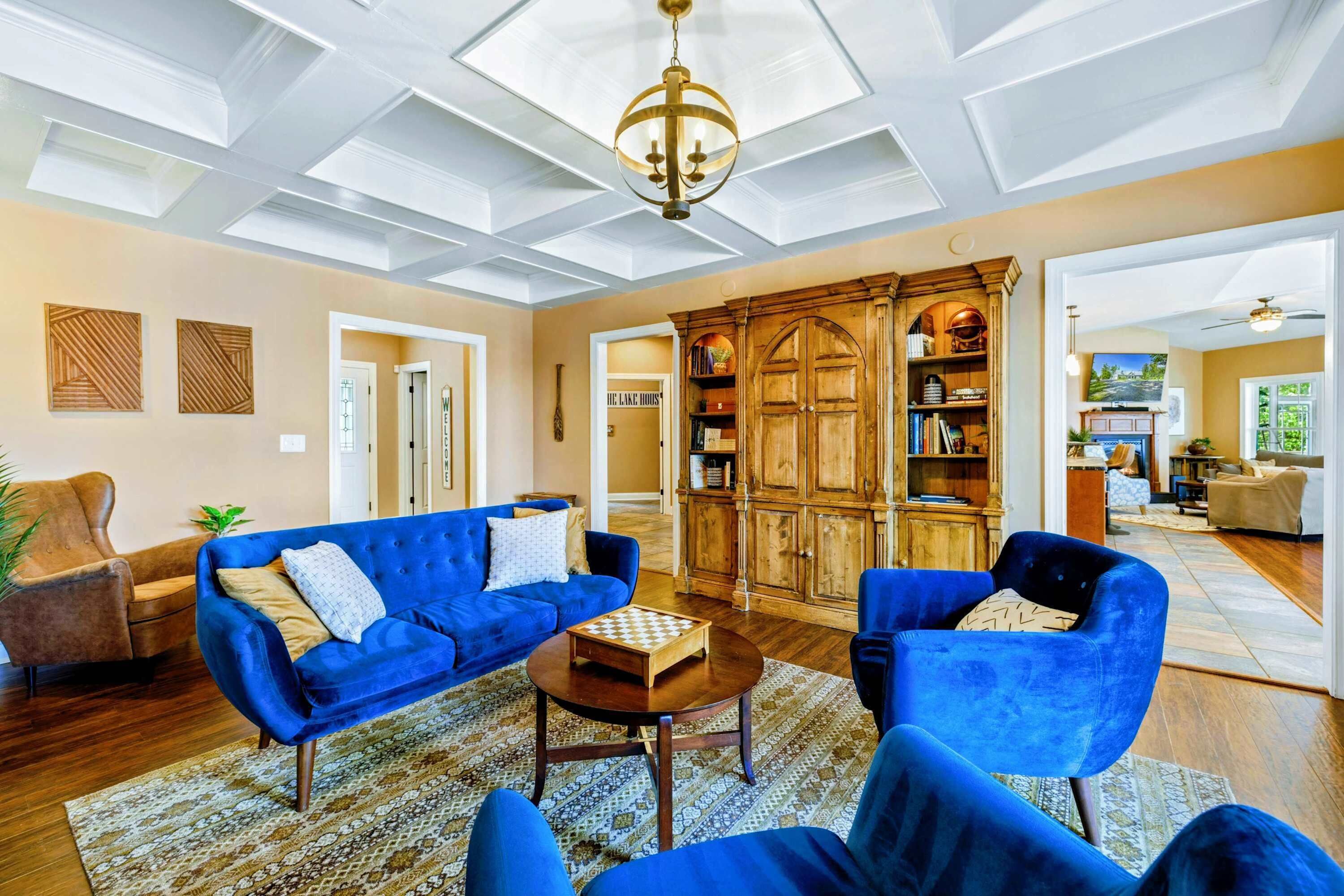 A spacious living room with a high ceiling, a chandelier, and a large wooden cabinet.