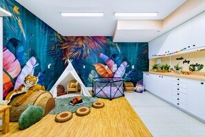Una habitación con un mural llamativo, una zona de juegos con piscina de pelotas, una tienda de campaña y un peluche de tigre.