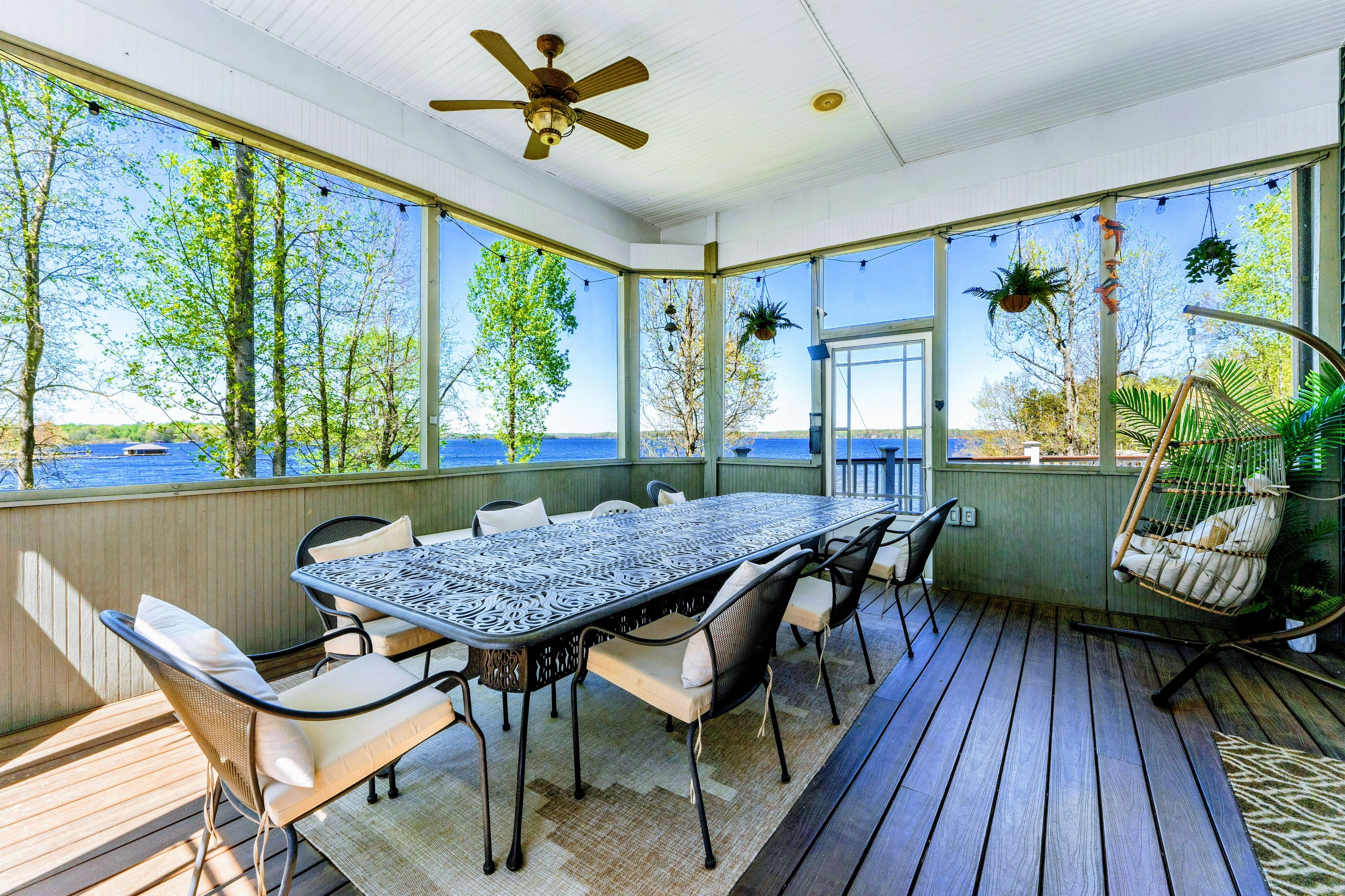 A covered outdoor dining area with a table and chairs, large windows, and a ceiling fan.