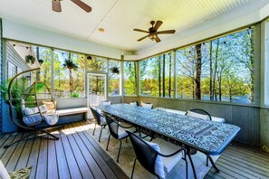A covered outdoor area with a long table, chairs, a swing chair, and hanging plants. - Huge 8BR Lakefront Lake Anna, Beach, Dock, Hot Tub (Bumpass)