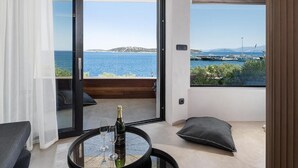 Varanda com vista para o mar e barcos, uma mesa com garrafa e copos, e um almofado.