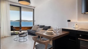 Uma cozinha moderna com área de jantar, grandes janelas com vista para o mar e um espaço de estar acolhedor com sofá e almofadas.