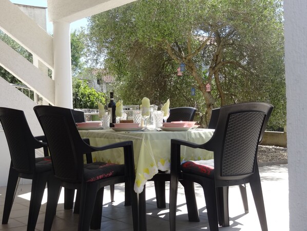 An outdoor dining area with a table set for four, surrounded by chairs, under a covered patio.