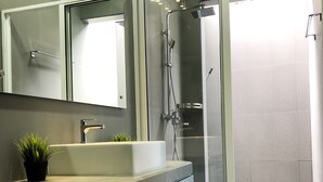 Un baño moderno con ducha envuelta en vidrio, un lavamanos con una planta y un espejo sobre él.