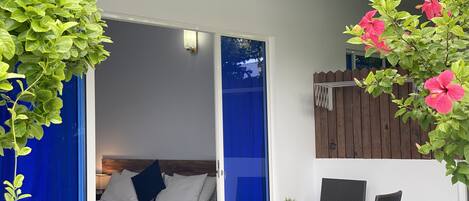 A room with a bed, a table, and chairs, a small plant, and a wooden fence outside.