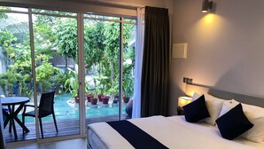 Habitación de hotel con una cama, una mesa con sillas y vistas a un jardín a través de un ventanal corredero.