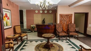 Um hall de entrada com balcão de recepção, cadeiras estampadas, uma mesa redonda e um lustre.