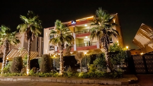 Um hotel com vários andares, varandas, palmeiras e arredores bem iluminados.