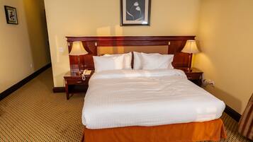 A hotel room with a large bed, two bedside tables, a wall-mounted air conditioner, and a framed picture above the bed.