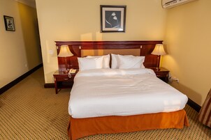 A hotel room with a large bed, two bedside tables, a wall-mounted air conditioner, and a framed picture above the bed.