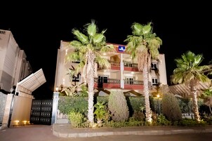 A multi-story hotel with a gated entrance, palm trees, and a well-maintained garden.