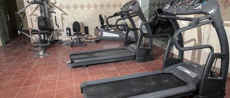 Un gimnasio con cintas de correr, máquinas de pesas y una banca.