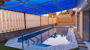Uma piscina com capa azul, cerca de metal e parede de pedra.