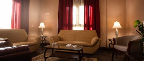 Una habitación de hotel con un sofá color beige, un sillón más pequeño, una mesita de centro y dos lámparas.