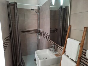 Een badkamer met een douche, een wastafel en een spiegel.