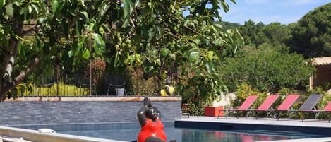 A swimming pool with a sculpture, surrounded by greenery and a stone wall.