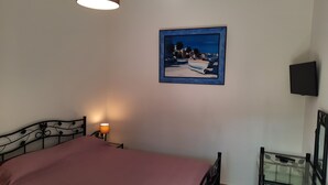 A bedroom with a bed, a nightstand, a lamp, a painting, and a TV.