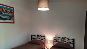 Una stanza con due letti singoli, una lampada a sospensione e un quadro appeso al muro.