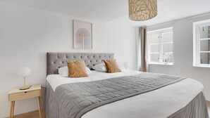 Un lit bien fait, avec une couette grise, une tête de lit capitonnée et deux oreillers marron.