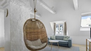 Un salon moderne avec un fauteuil suspendu, un canapé, une petite table et une vue sur la ville par une fenêtre.