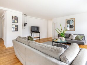 A modern living room with a grey sofa, a small coffee table, a TV on a stand, and abstract art on the walls. - Regent 3 - Popular 3-Bdr Apt with Balcony in Centre (København)