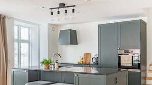 A modern kitchen with a central island, grey cabinets, a built-in oven, and a window with curtains. - Regent 3 - Popular 3-Bdr Apt with Balcony in Centre (København)