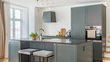 A modern kitchen with a central island, grey cabinets, a built-in oven, and a window with curtains.